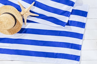 Lifestyle image of Mainstays Blue Cabana Stripe Beach Towels with beach hat and star fish