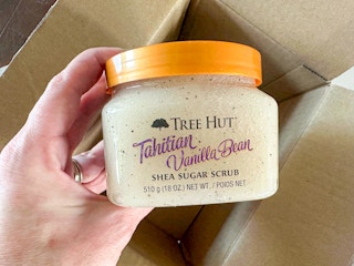 Hand holding Tree Hut Shea Sugar Scrub over Amazon box