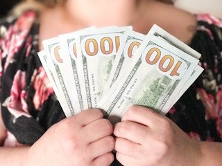 woman holding several one hundred doklar bills.
