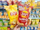 hand holding two bags of potato chips in chip aisle