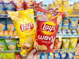 hand holding two bags of potato chips in chip aisle
