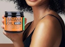 a person holding a jar of batana hair oil 