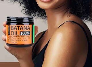a person holding a jar of batana hair oil 