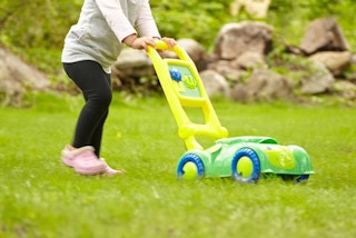 stock photo of melissa and doug snappy turtle lawn mower being pushed by little girl on grassy yard