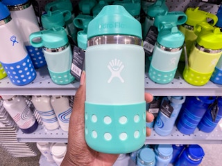a hydroflask being held in front of a display of other hydrflasks