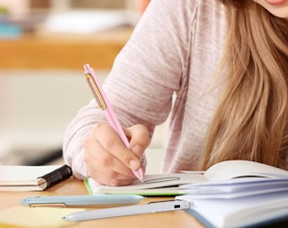 a person writing with a pink pen on a desk