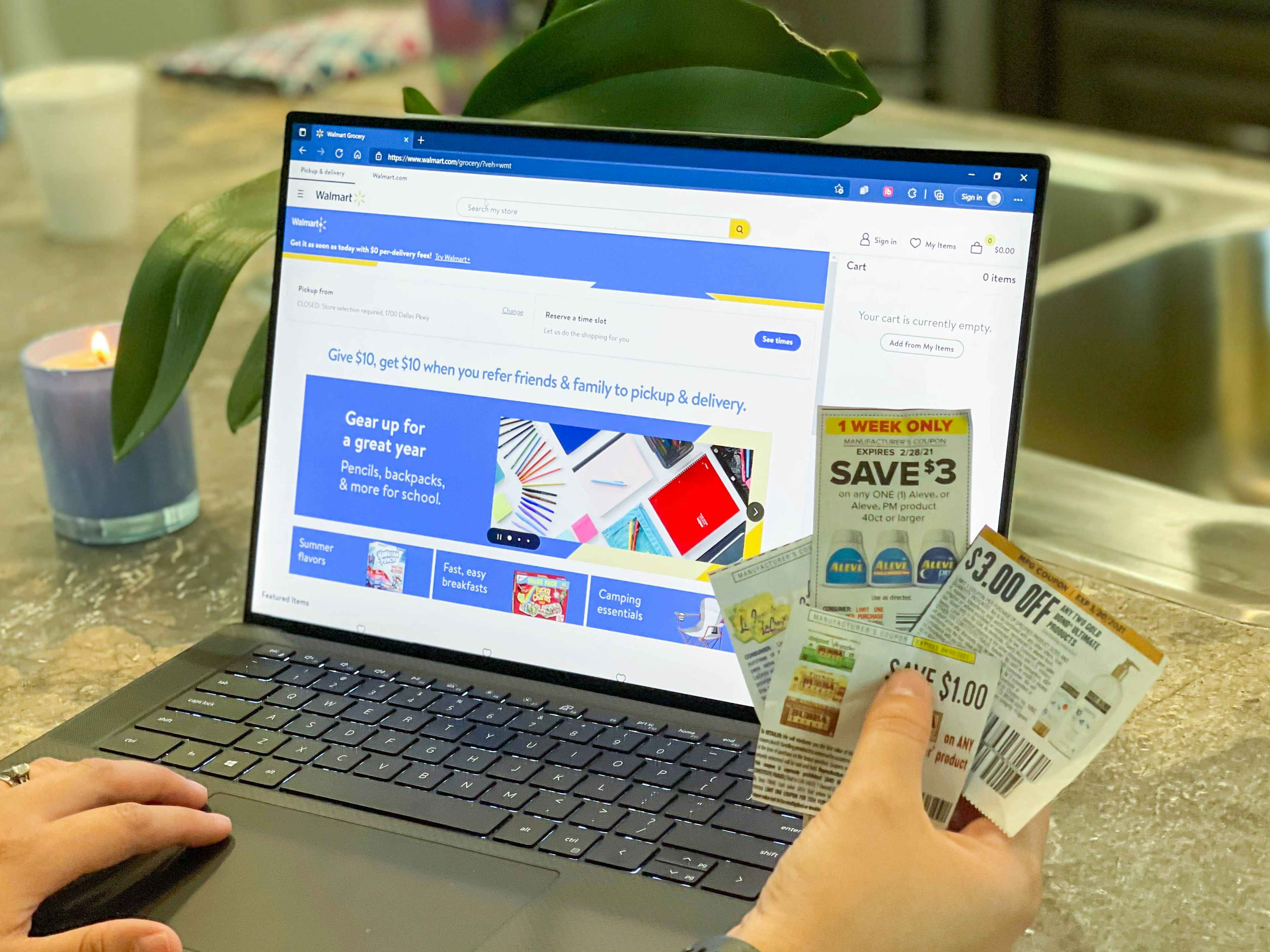walmart.com online on laptop with coupons being held in front of it.