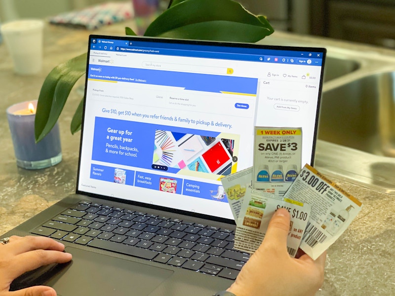 walmart.com online on laptop with coupons being held in front of it.