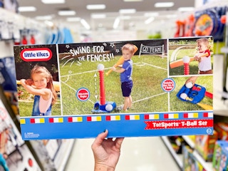 a hand holding a box with a kid's t-ball set on it 