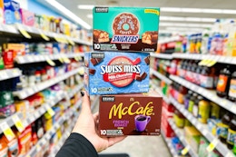 person holding 3 boxes of kcups in an aisle