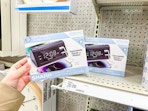 hand holding a sharp dual alarm clock in front of a target shelf
