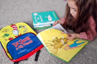 A child laying on the floor reading The Big Honey Hunt next to some more Dr. Seuss books and a Dr. Seuss backpack.
