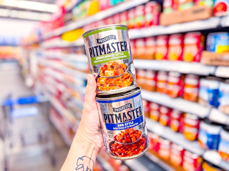 hand holding two cans of progresso pitmaster soups in walmart aisle