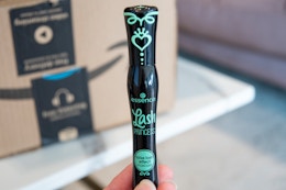 A hand holding Essence Lash Princess Mascara in front of an Amazon box.