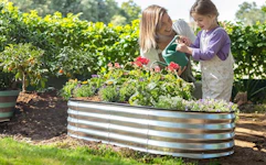 a mom and daughter watering flowers in a garden bed