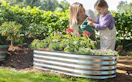a mom and daughter watering flowers in a garden bed
