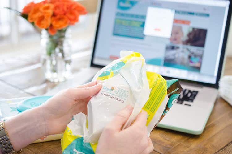 A person looking at the code on the inside of a pampers diapers package. A laptop computer is in the background with pampers website open...