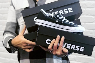 person holding several boxes of converse and black chuck taylor all-star sneakers