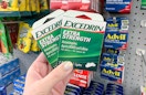hand holding two small green and white boxes of excedrin extra strength tablets in front of other pain relievers at dollar tree