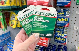 hand holding two small green and white boxes of excedrin extra strength tablets in front of other pain relievers at dollar tree