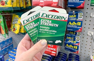 hand holding two small green and white boxes of excedrin extra strength tablets in front of other pain relievers at dollar tree