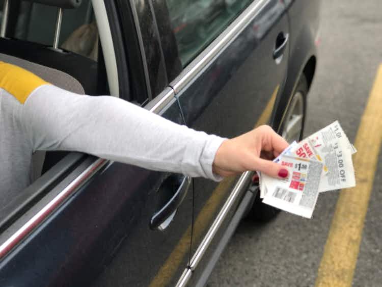 Hand holding paper coupons out of a car window