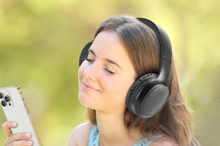 A young girl wears headphones and holds a cell phone, looking blissful