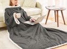 a person sitting on a floor with a laptop wearing a wearable blanket