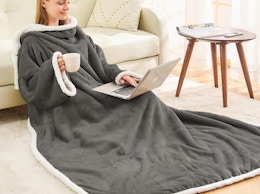 a person sitting on a floor with a laptop wearing a wearable blanket