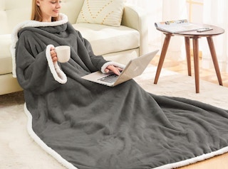a person sitting on a floor with a laptop wearing a wearable blanket