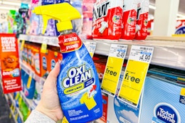 person holding a bottle of oxiclean stain remover by a buy 1 get 2 free sign