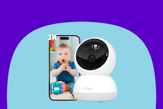 A smartphone has the image of a baby playing. The indoor security camera is next to it, a white sphere on a white and grey base.