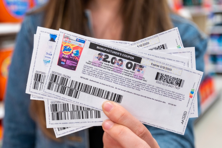 A person holding out a stack of manufacture coupons. The coupon on top is for $2 off Tide Pods.