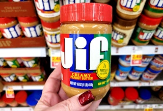 A person holding a ja of Jif peanut butter in fornt of a store shelf with other jars of Jif peanut butter.