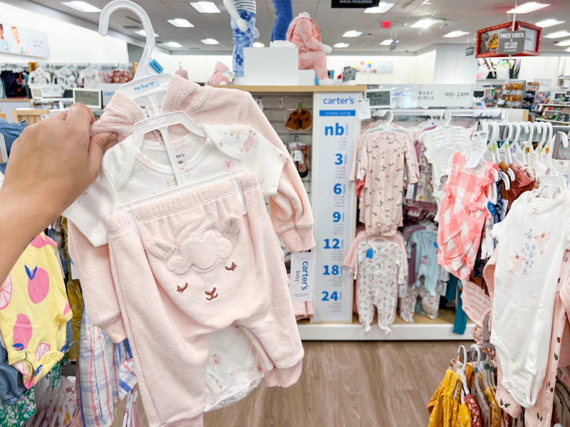 a hand holding up a carter's three piece set in the baby clothing area at kohl's