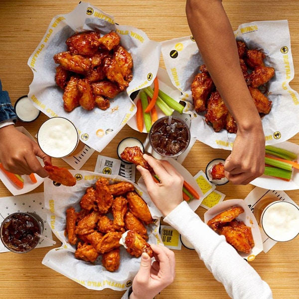 People grabbing food from several plates sitting on a table.