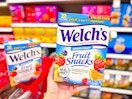 hand holding a welch's fruit snacks value pack in front of a target cart
