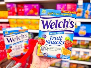 hand holding a welch's fruit snacks value pack in front of a target cart