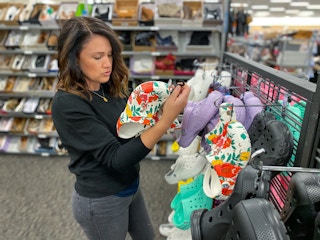 A woman looking at a pair of Crocs in front of a Croc display at a shoe store.