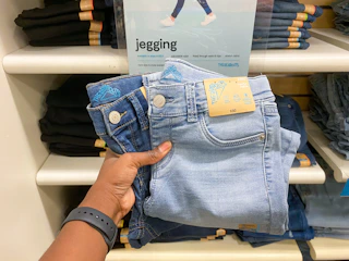 someone holding up a pair of kids jeans from a display of other jeggings