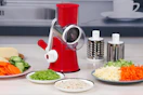 lifestyle image of a rotary cheese and vegetable grater on a counter with a variety of food