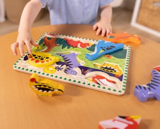 a kid playing with a wooden dinosaur puzzle