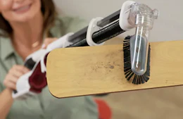 a person using a handheld vacuum to clean a ceiling fan 