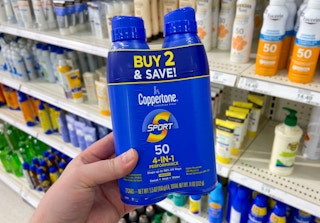 hand holding a two-pack of coppertone sunscreen spray in a store