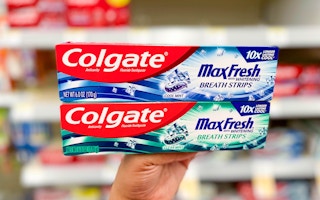 Hand holding two boxes of Colgate Maxfresh toothpaste in aisle