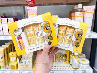 Hand holding two Burt's Bee's Tips And Toes Kit in front of other Burt's Bees products