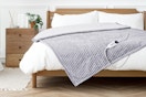 Lifestyle image of the Justlet heated blanket in light gray (laid out on bed)