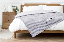 Lifestyle image of the Justlet heated blanket in light gray (laid out on bed)