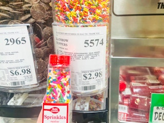 Someone holding a bottle of sprinkles in front of a bulk sprinkle bin at WinCo