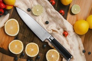 A chef knife on a cutting board with a cheesecloth and sliced fruit